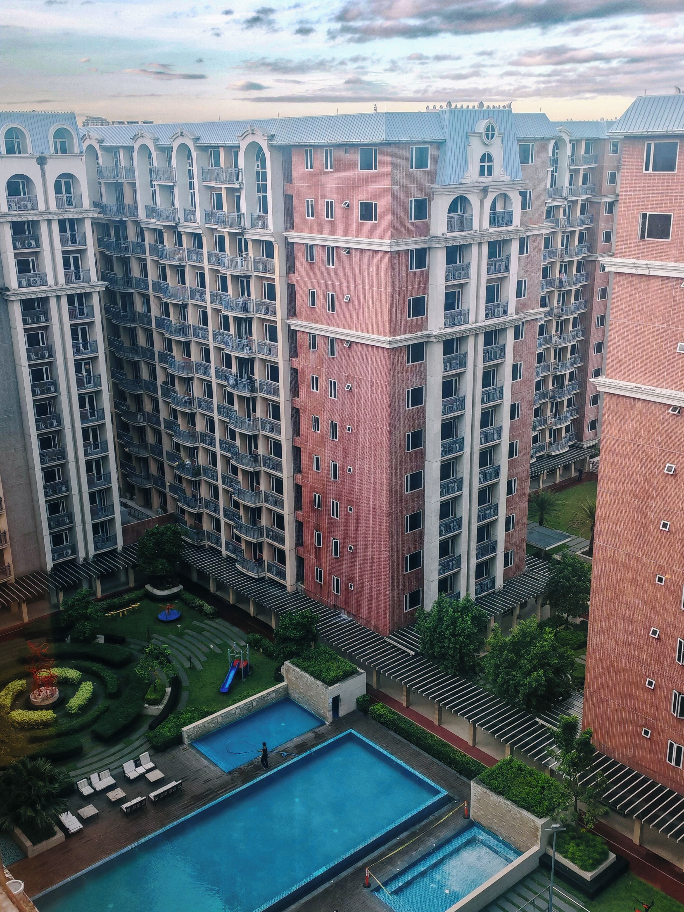 A high-rise residential building with multiple balconies, a swimming pool, and a landscaped garden area.