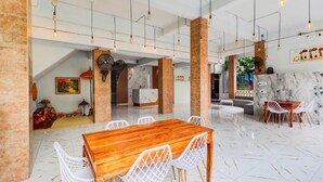 Un comedor amplio con una mesa de madera y sillas blancas, suelo de mármol y lámparas colgantes.
