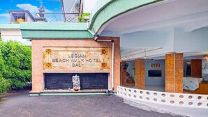 Exterior del Hotel Legian Beach Walk Bali, destacando una entrada imponente con una estatua de piedra, una vista despejada de la fachada y una zona circundante bien cuidada.
