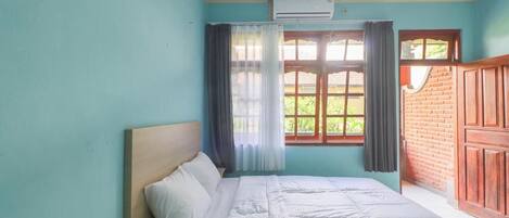 A bedroom with a bed, a window with curtains, and a brick wall.