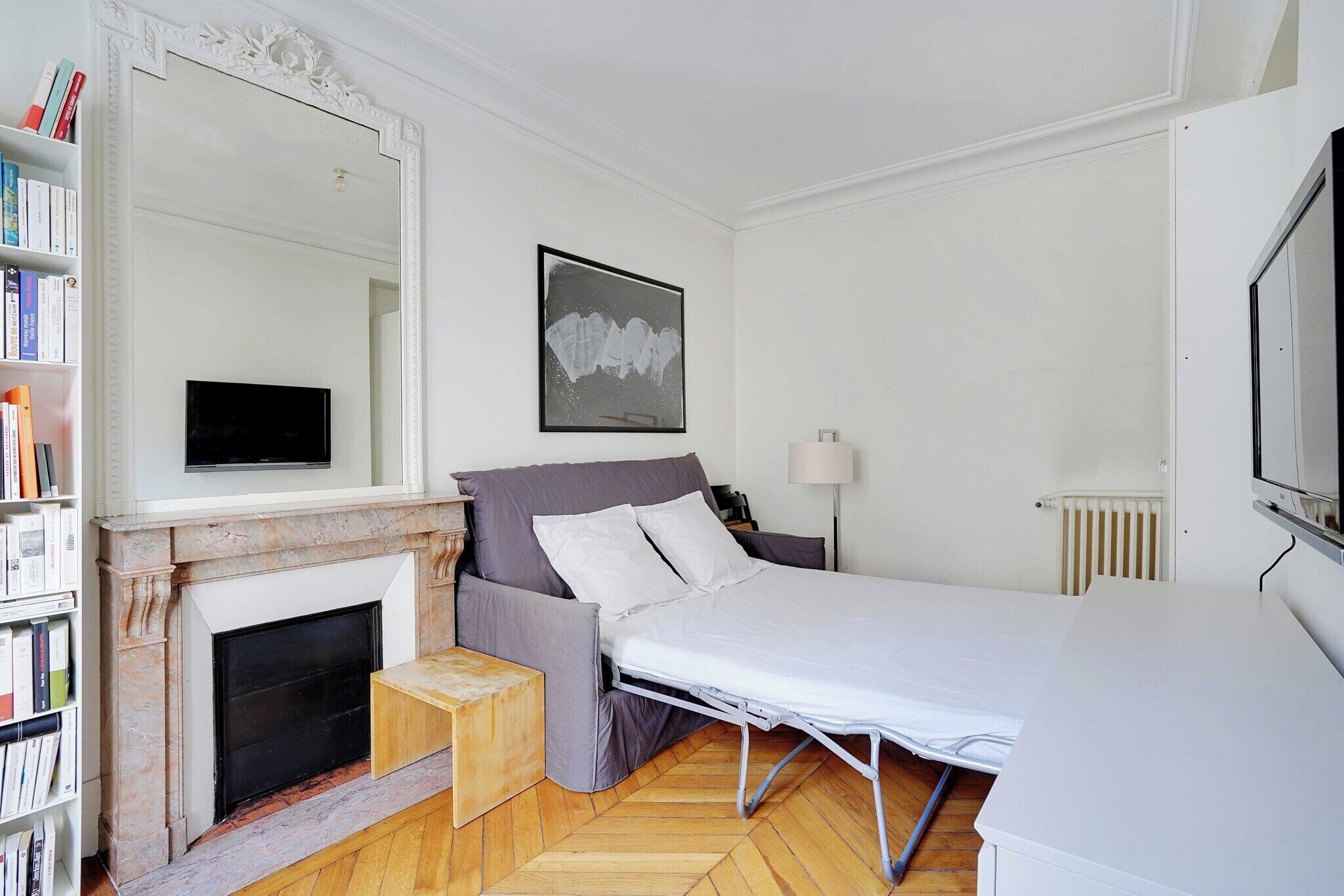 A bedroom with a bed, a fireplace, a bookshelf, a framed picture, and a radiator.