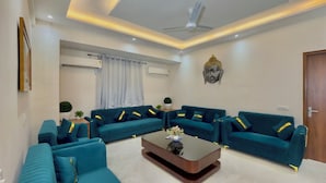 A modern living room with teal sofas, a central coffee table, and a Buddha statue on the wall. - Hotel The Tusk (Rishikesh)