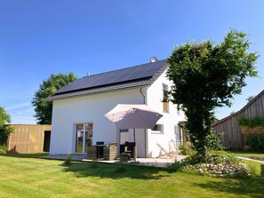 A two-story house with a patio, a large umbrella, and a wooden fence. - Riedlodge Lake Constance-Upper Swabia Holiday Home (Guggenhausen)