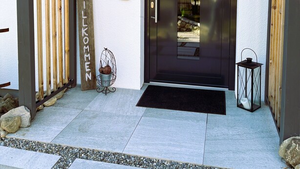 A modern entrance with a dark door, a wooden gate, a metal lantern, and a welcome mat. - Riedlodge Lake Constance-Upper Swabia Holiday Home (Guggenhausen)