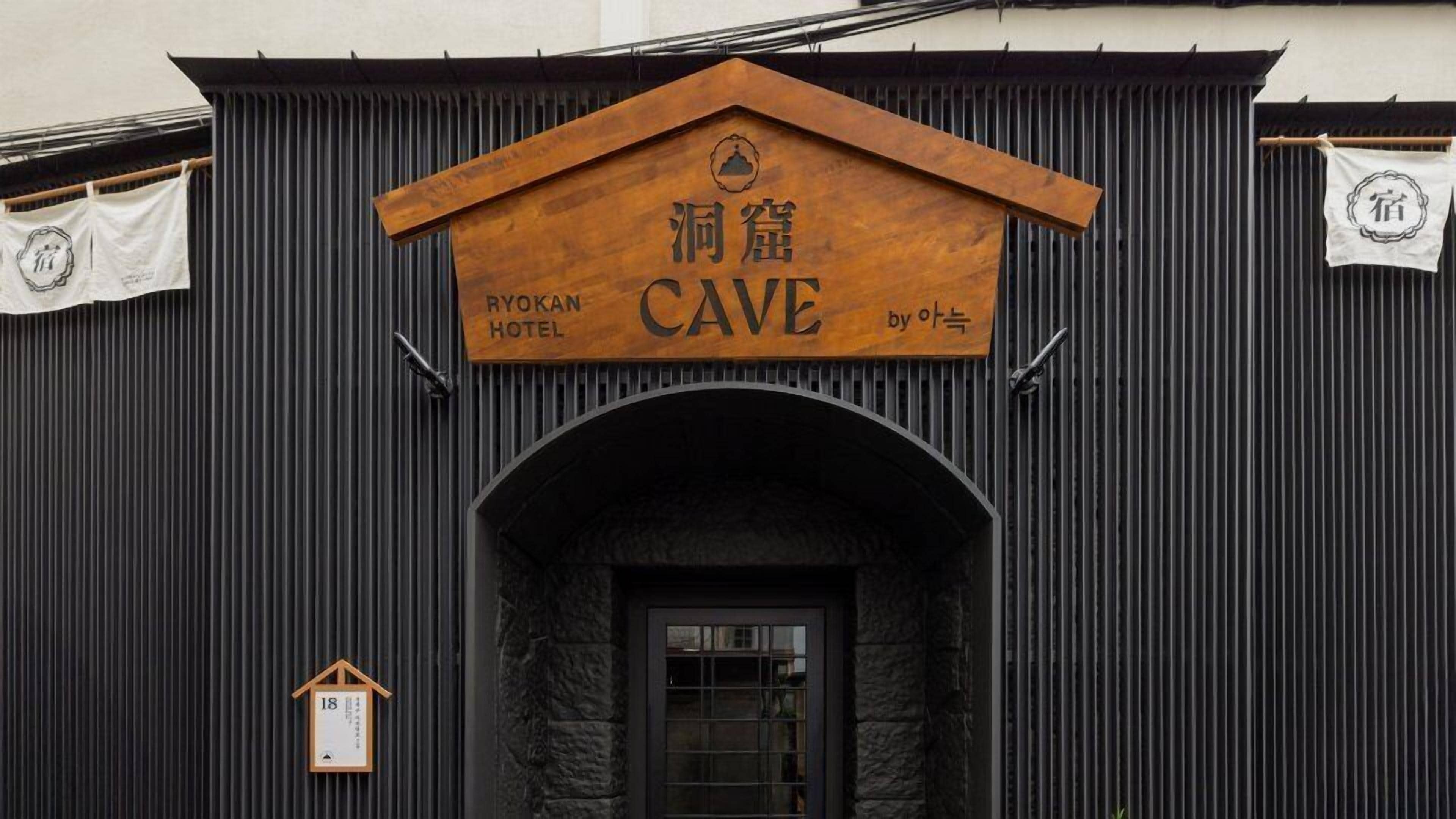 A hotel entrance with a wooden sign reading "Ryokan Cave by Oat".