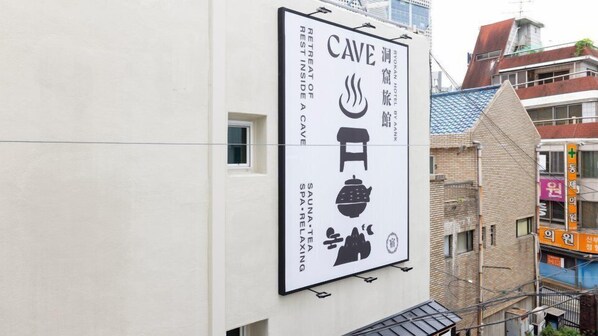 Une enseigne verticale faisant la publicité d’un séjour bien-être, avec des symboles représentant un sauna, une source d’eau chaude et des activités de détente.