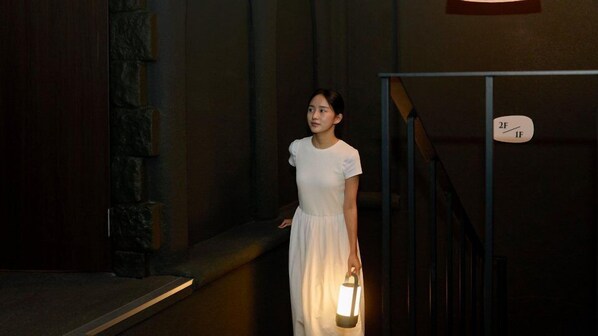 A person in a white dress holding a lantern, standing in a dimly lit hallway with stone walls and a metal railing. - Cave Ryokan Hotel by Anook Sungshin Univ. (Seoul)