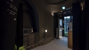 A dimly lit hallway with a microwave on a counter, a stone ledge, and a door leading to a room with a window.