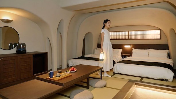 A hotel room with two beds, a wooden desk, a mirror, and a nightstand with a lamp.