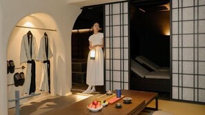 A room with a wooden table, a person holding a light, and a seating area with a view through a shoji screen.