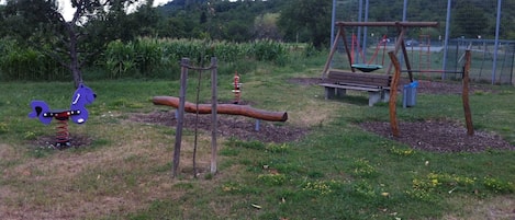 Un parque infantil con columpios, un sube y baja y un tobogán.