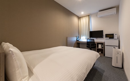 A hotel room with a bed, a desk with a computer, a television, and a microwave.