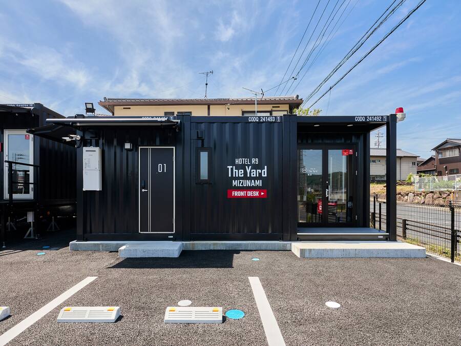 A compact hotel named "The Yard Mizunami" with a front desk area, a small outdoor seating space, and a visible entrance.