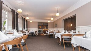 Un restaurant avec de nombreuses tables dressées pour le service, des chaises en bois et des lampes suspendues.