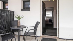 Un petit espace patio avec une table et deux chaises, un pot de fleurs et une porte-fenêtre donnant sur l’intérieur.