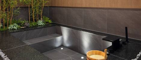 Un bagno moderno con una vasca da bagno nera, uno sgabello in legno e piante di bambù.