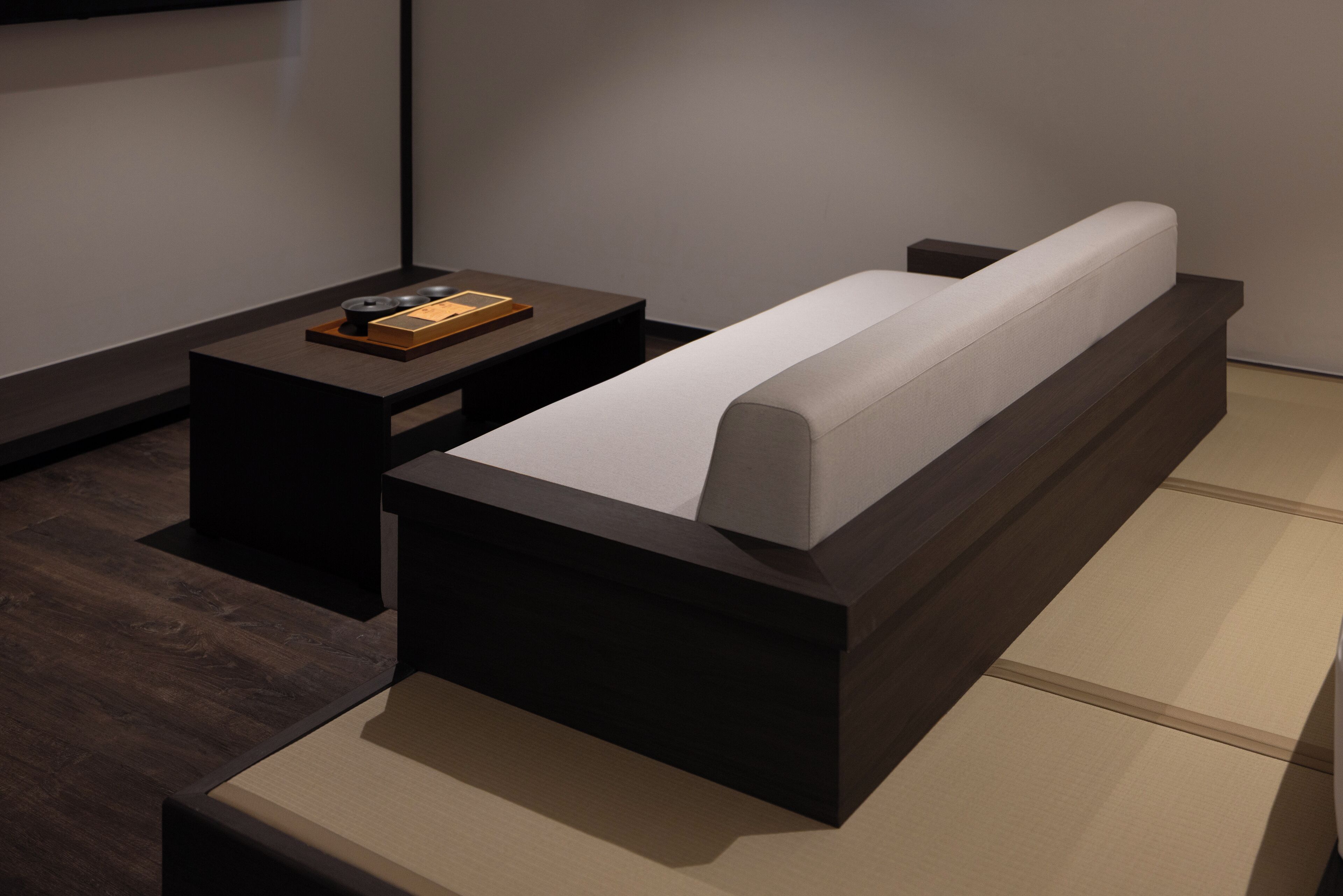 A modern room with a dark wooden bed frame, a small bedside table, and a light-colored mattress.