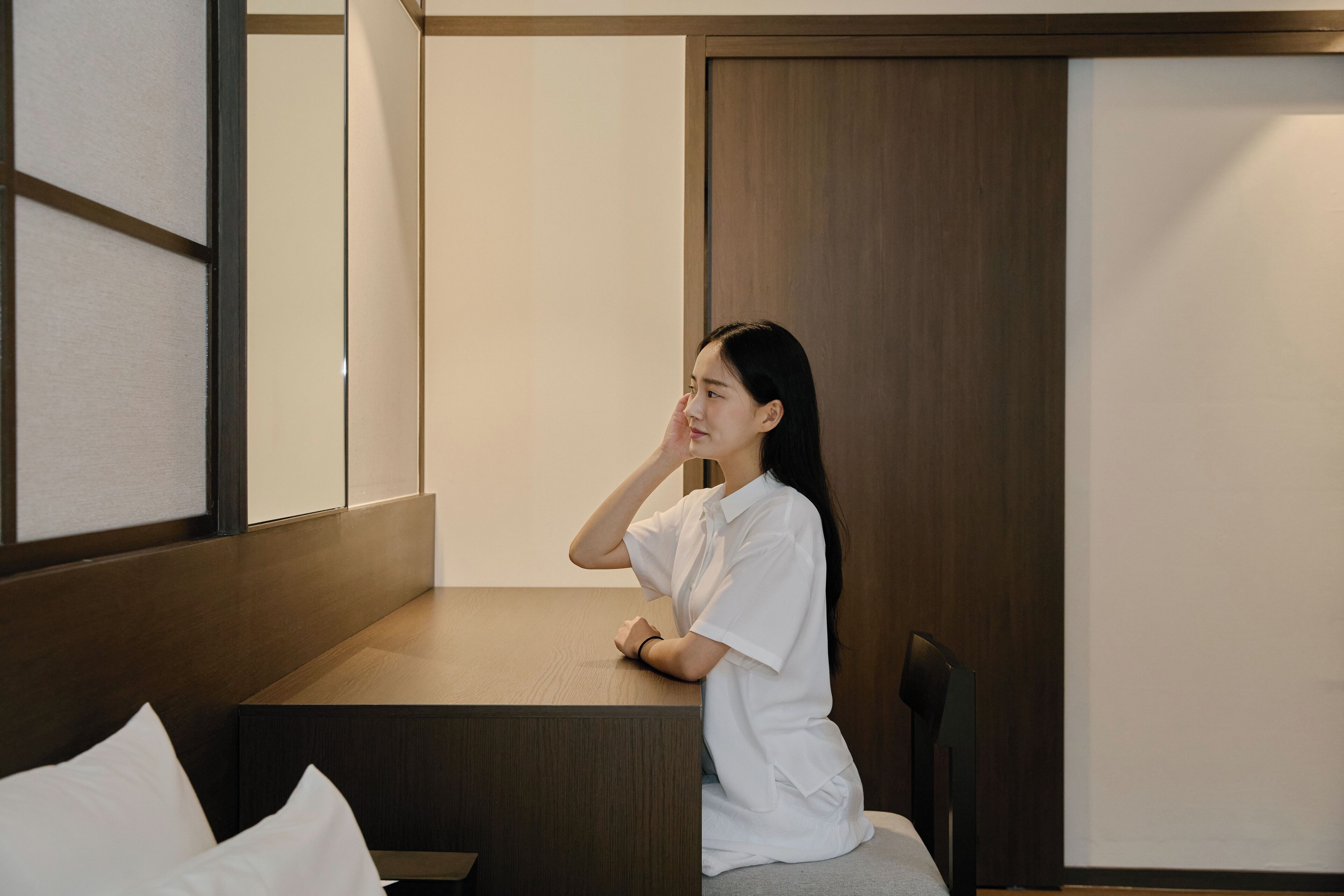 A person sitting at a wooden table in a room with a sliding door and a view of a building outside.