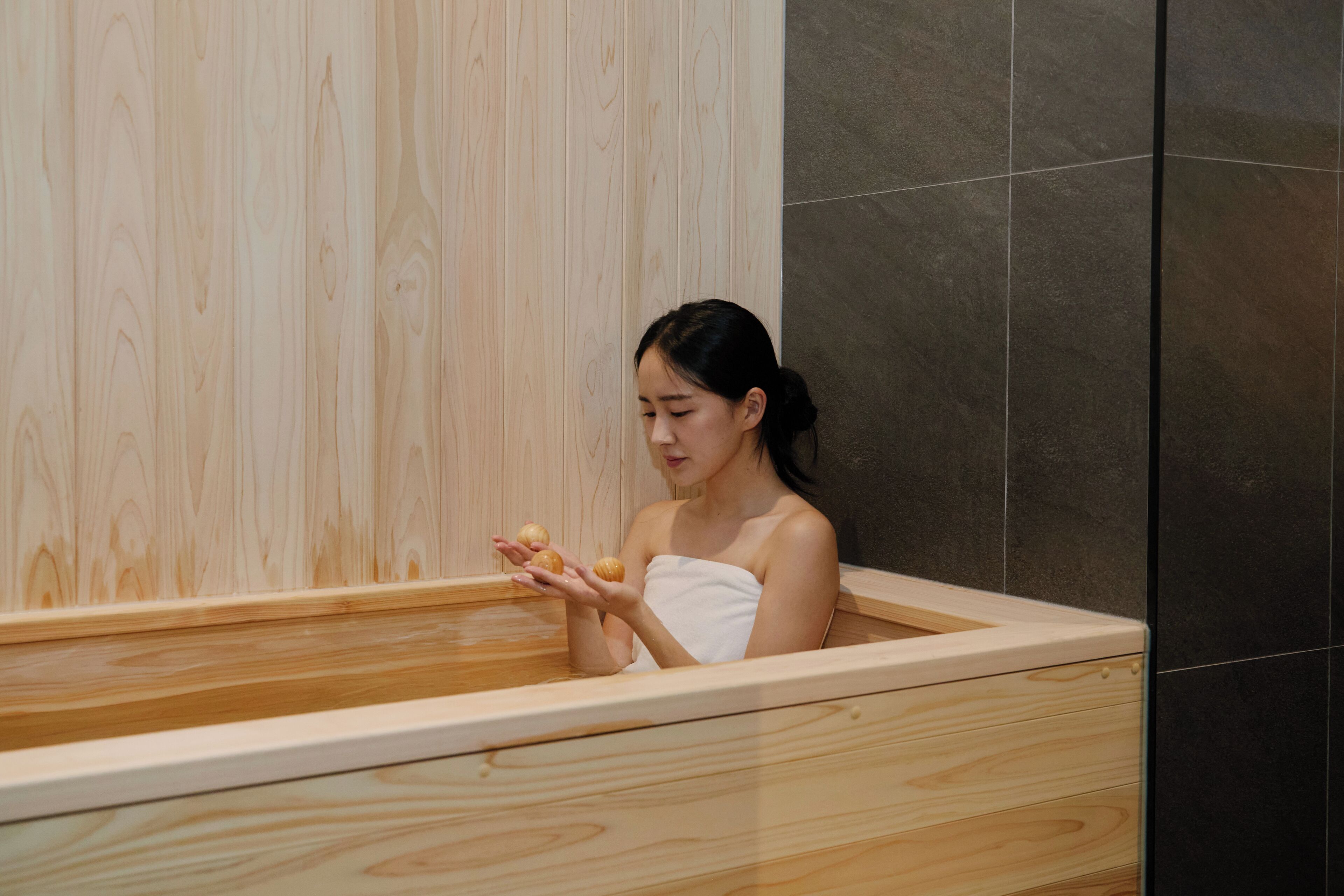 A person in a wooden bathtub with a towel wrapped around their body.