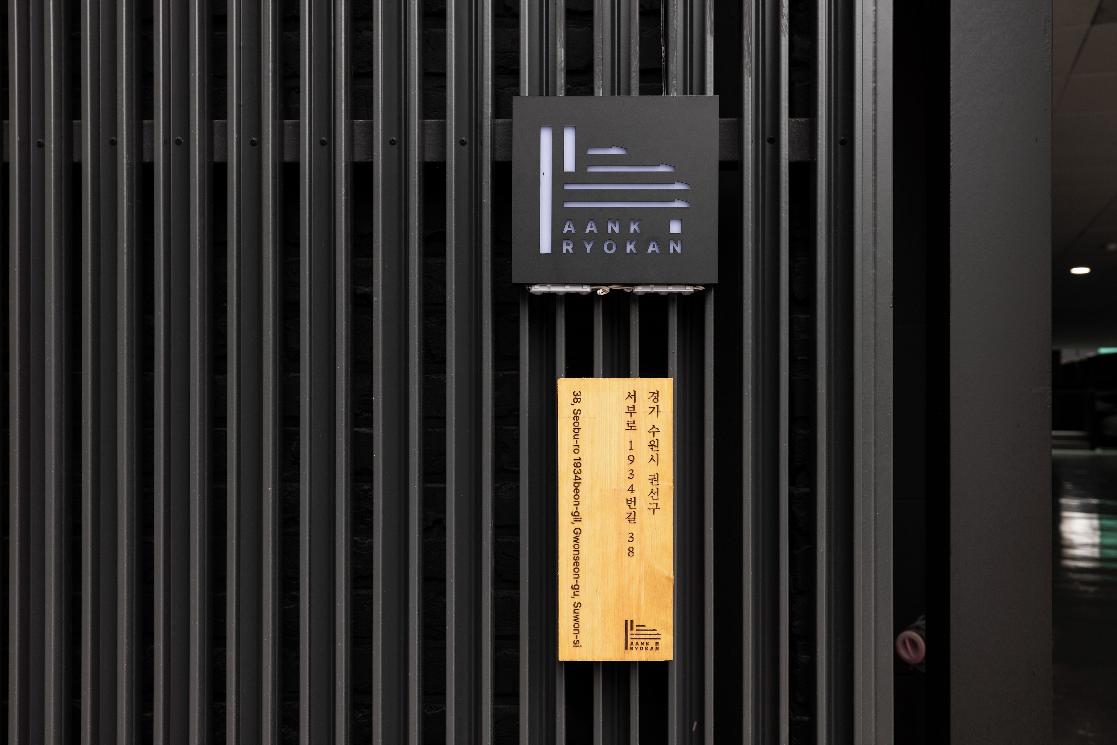 A sign for AANK Ryokan with a wooden plaque below it.