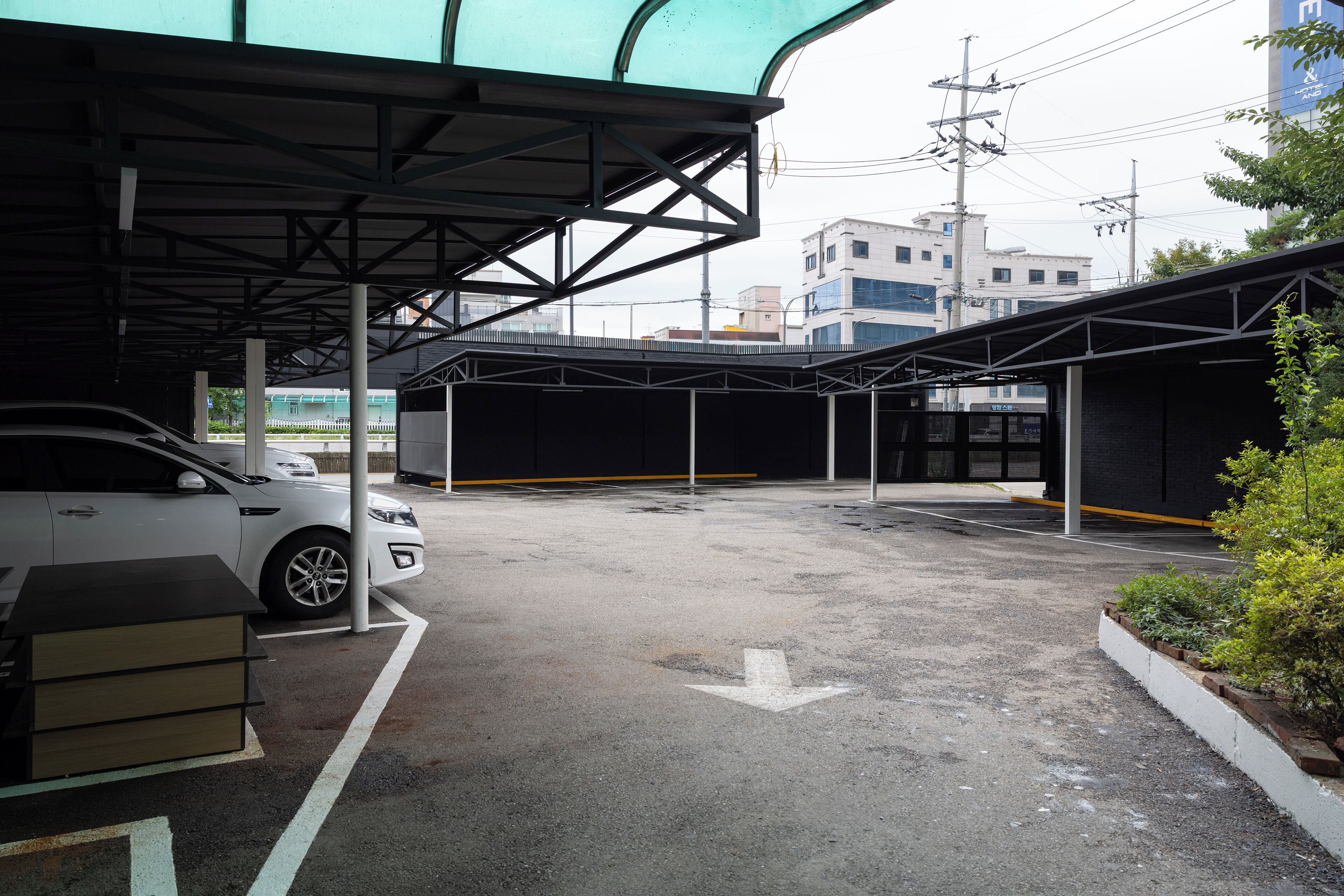 Un espace de stationnement avec une voiture blanche, une poubelle et une flèche directionnelle peinte au sol.