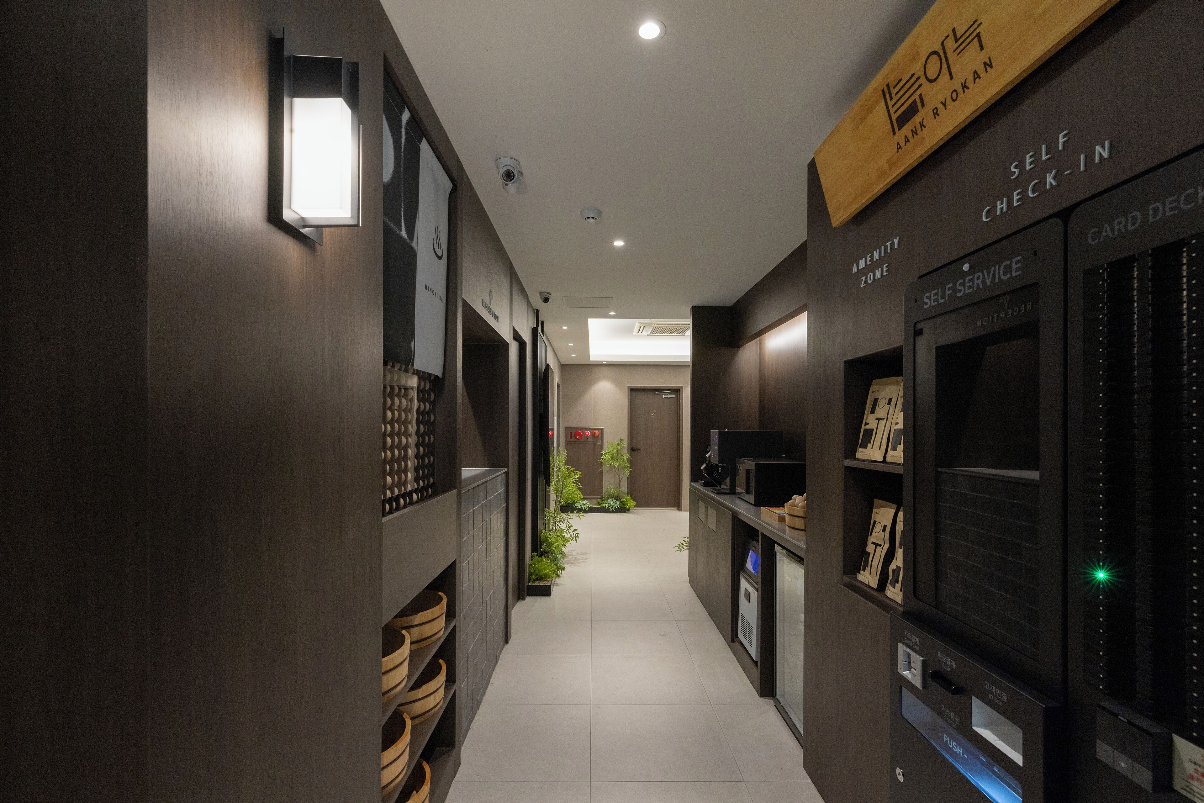 Un couloir d’hôtel moderne doté de bornes d’enregistrement en libre-service, d’une caméra de surveillance et d’un petit jardin intérieur.