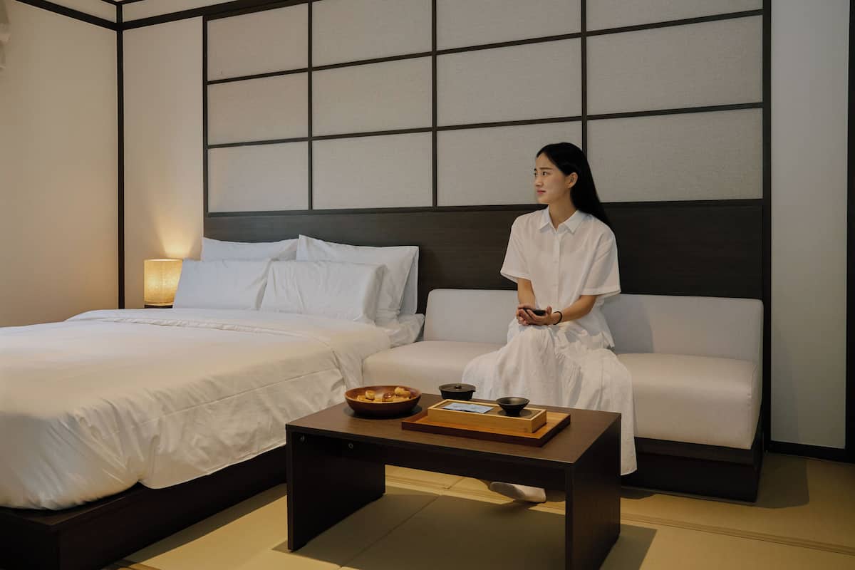 A hotel room with a bed, a sofa, and a small table with a bowl and a tray.