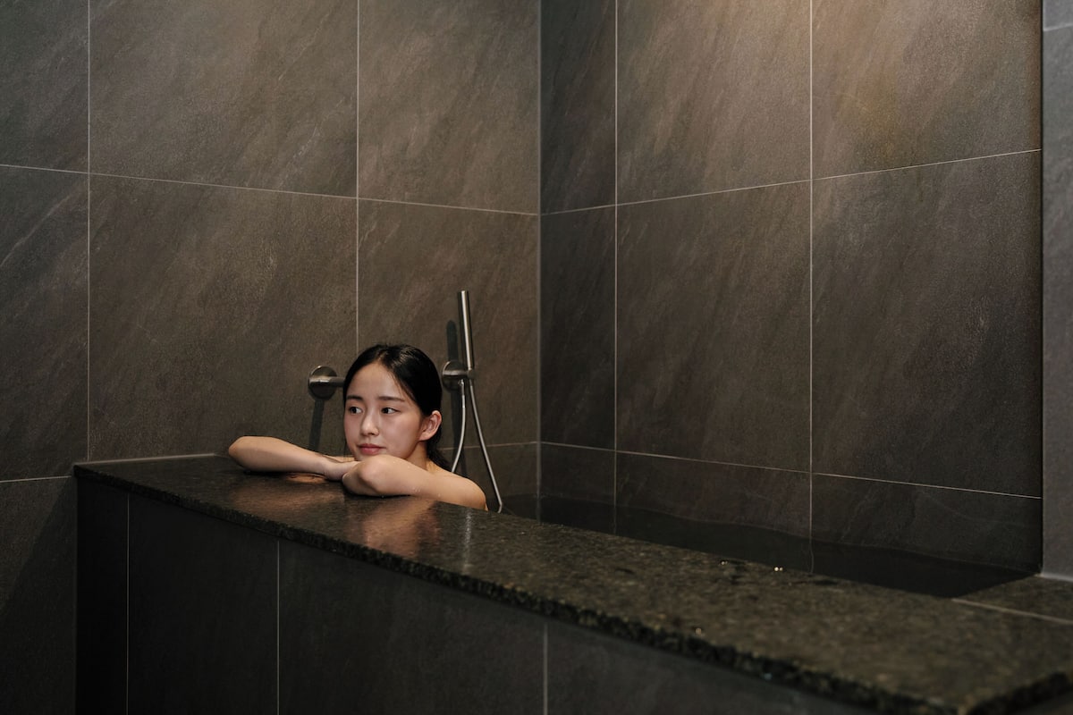 A person relaxing in a bathtub with a modern design, surrounded by dark tiles.