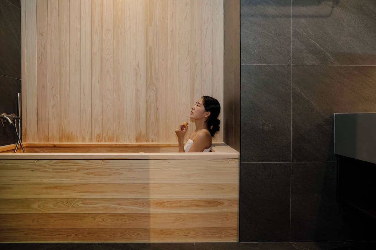 A woman in a wooden bathtub with a towel, a wooden panel wall, and dark tiled flooring.