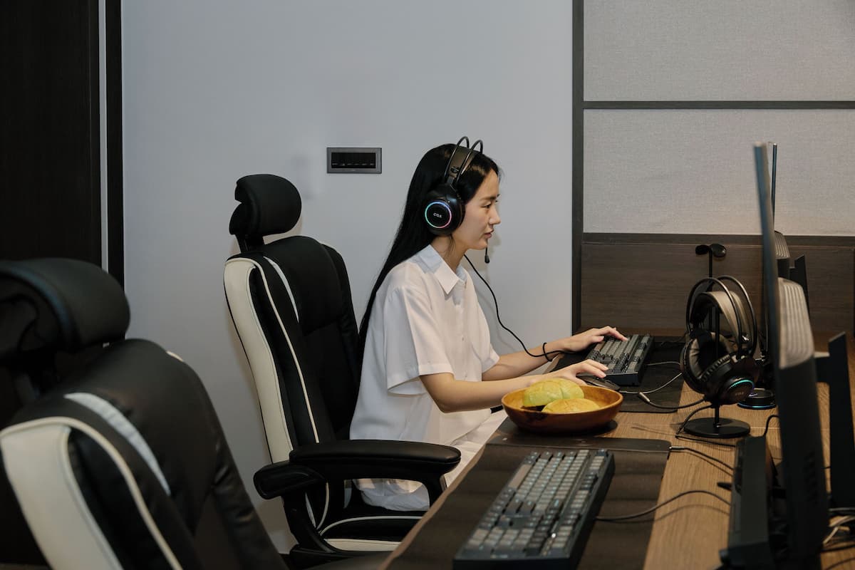 A person seated at a desk with a computer, headphones, and a bowl of food.