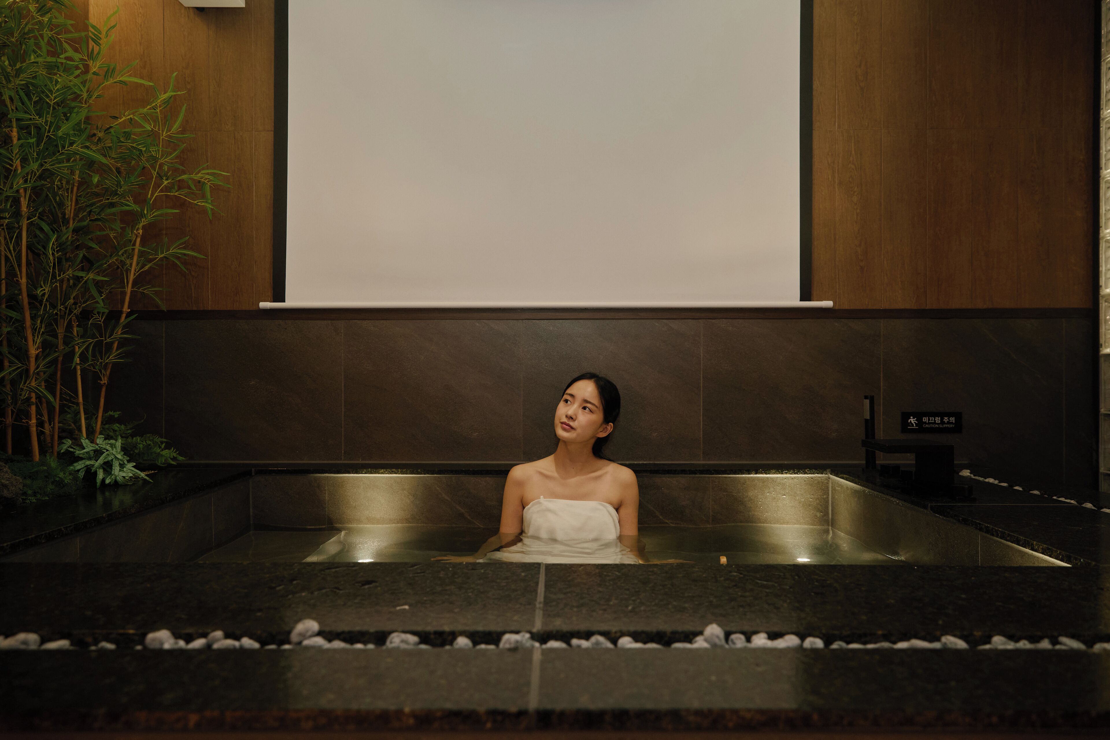 A person in a spa bath with a wooden wall and a plant to the left.