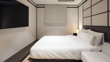 A modern hotel room with a large bed, a flat-screen TV mounted on the wall, and a bedside table with a lamp.