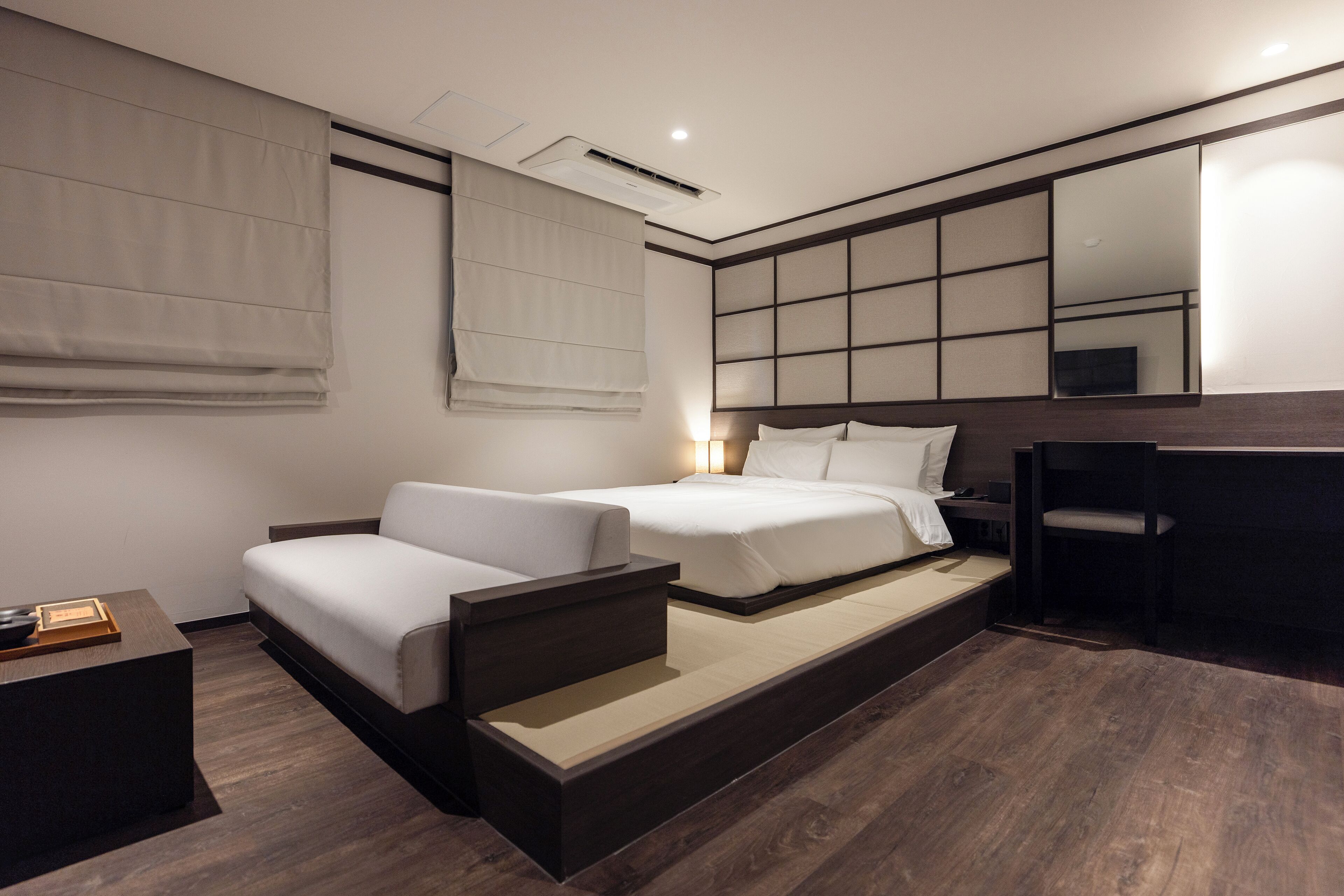 A modern hotel room with a sofa bed, a desk, and a large mirror.