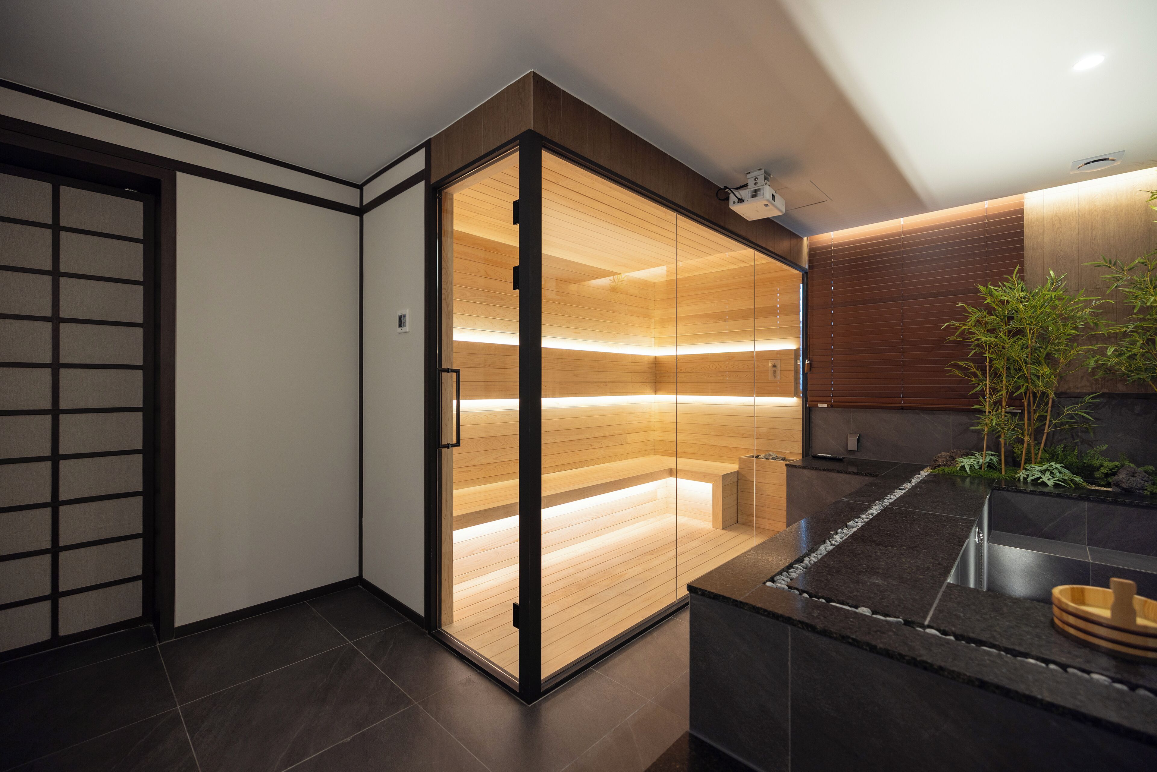 A modern interior with a sliding glass door leading to a wooden interior, a dark tiled floor, and a small plant on the counter.