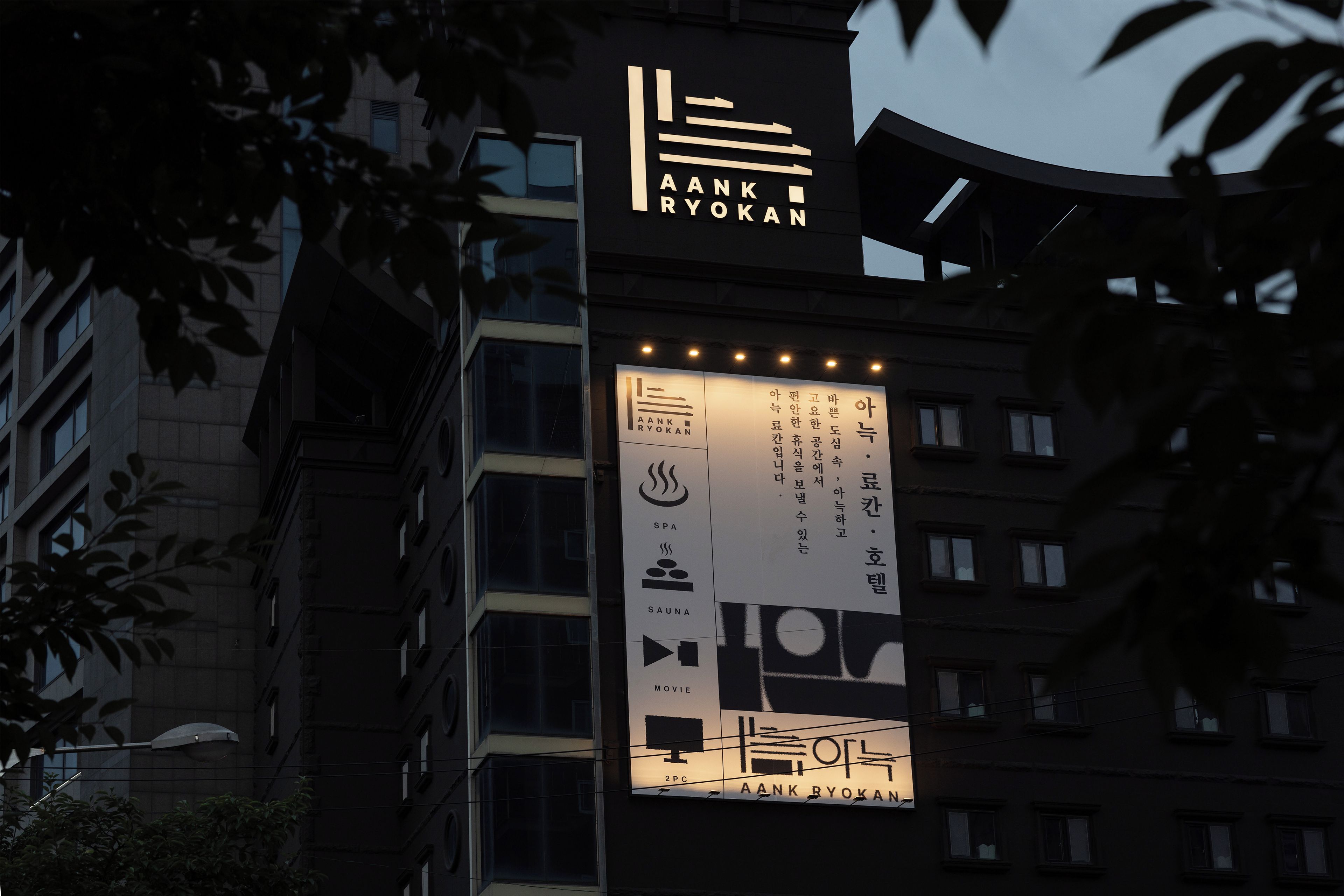 A building with a sign for 'AANK RYOKAN' featuring amenities like spa, sauna, and movie room.