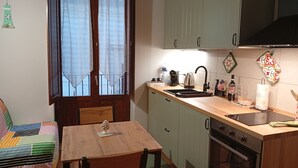 A compact kitchen with a wooden table and chairs, a built-in oven, and a window with curtains. - Borgo Sant'Antonio 14B (Siracusa)