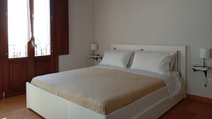 A bedroom with a bed, a nightstand, a wall-mounted air conditioner, and a window with curtains. - Borgo Sant'Antonio 14B (Siracusa)