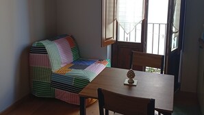 A room with a wooden table and chairs, a colorful quilted sofa, and a window with curtains. - Borgo Sant'Antonio 14B (Siracusa)