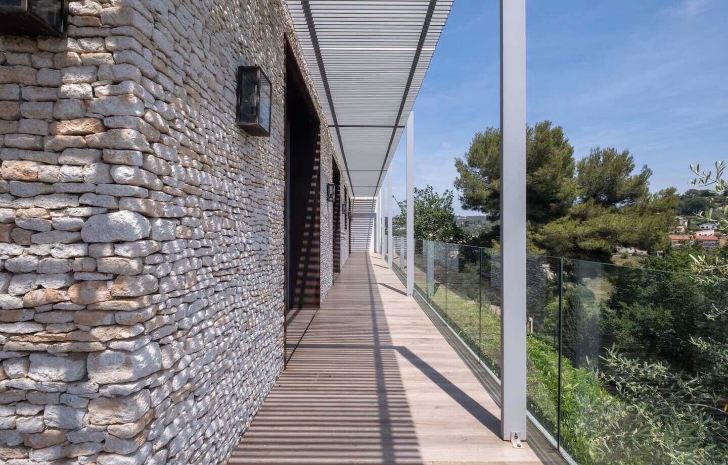 A stone building with a wooden deck and a glass railing overlooking a landscape.