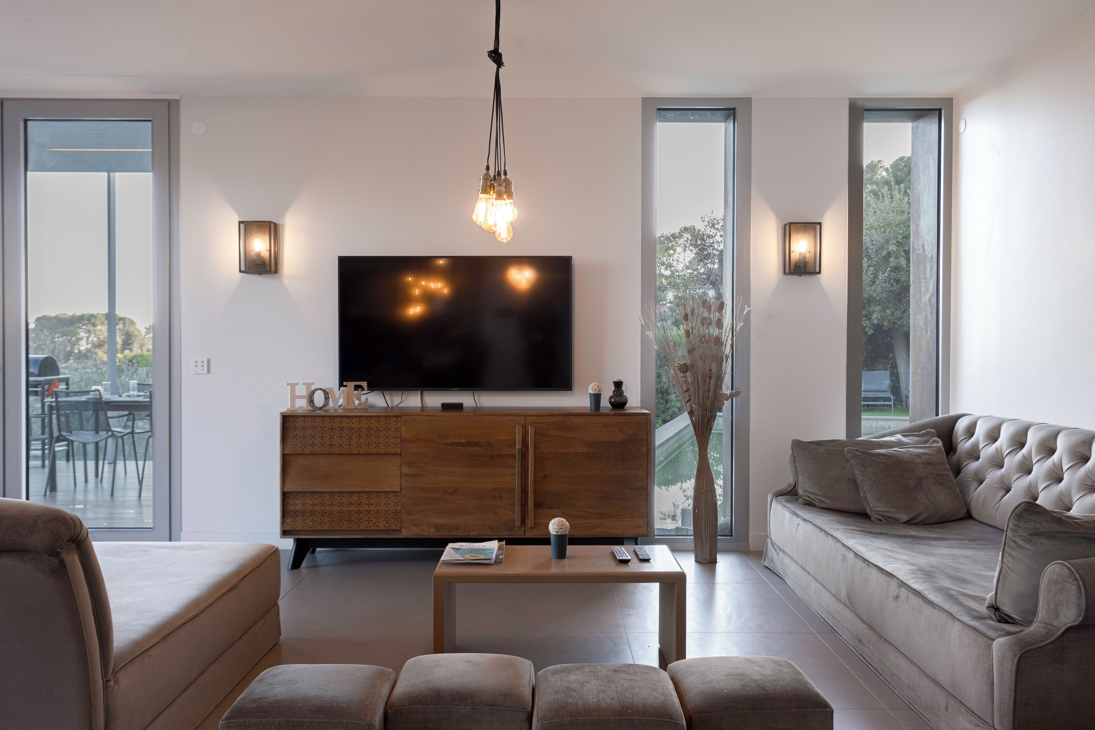 Un salon moderne avec un téléviseur à écran plat, un meuble en bois, un canapé et des poufs.