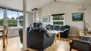 Een ruime woonkamer met een zwarte leren bank, een houten salontafel en uitzicht op groen.