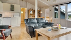 Een moderne keuken met witte kastjes, een zithoek met een houten tafel en stoelen, en een leren bank.