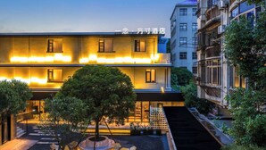 A modern hotel with a well-lit entrance, outdoor seating area, and a small tree in the center. - Yi Nian Fangcun Hotel (Nanchang)