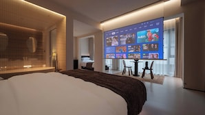 A modern hotel room with a large bed, a TV displaying various channels, and a glass partition separating the room from the hallway. - Qi Yi Nanxu Pavilion Homestay (Kunming)
