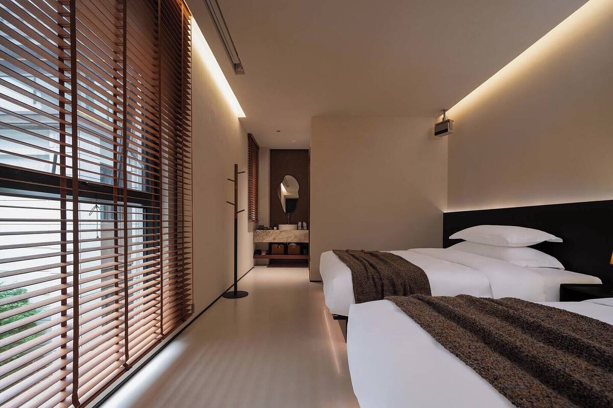 Une chambre d’hôtel moderne dotée d’un grand lit, d’un lit plus petit et d’un coin salon avec un banc.