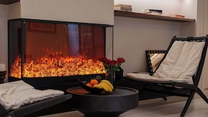 A modern living room with a large fireplace, a round coffee table with fruits and flowers, and a black chair. - Qi Yi Nanxu Pavilion Homestay (Kunming)