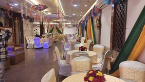 A banquet hall with round tables, white chairs, and hanging floral decorations. - HOTEL SHHAURYA  (New Delhi)