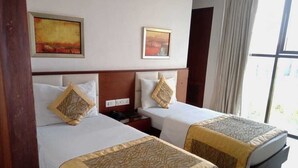 A hotel room with two beds, each with a patterned bedspread, a nightstand, and a wall-mounted telephone. - HOTEL SHHAURYA  (New Delhi)