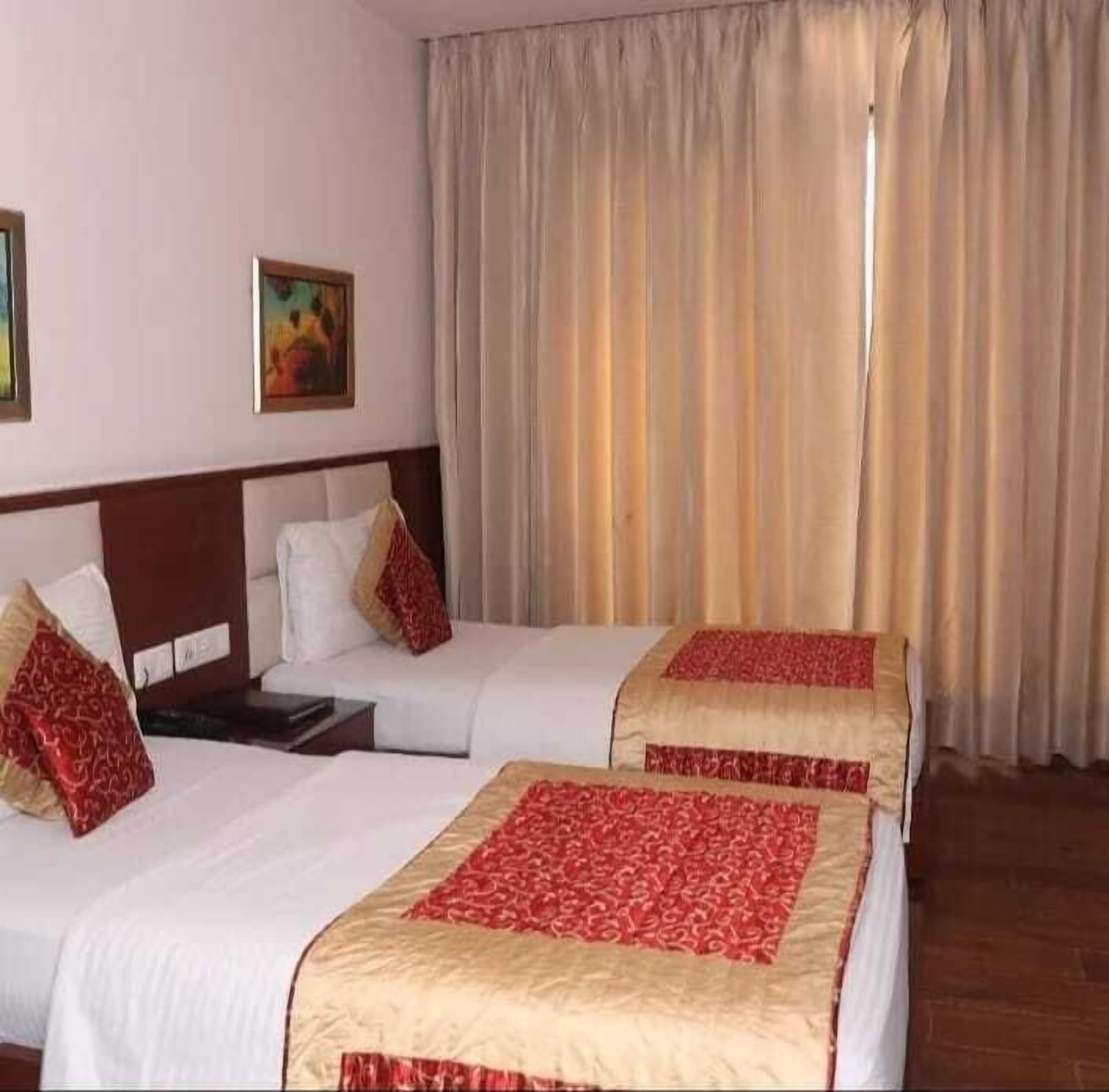 A hotel room with two beds, beige curtains, and a painting on the wall.