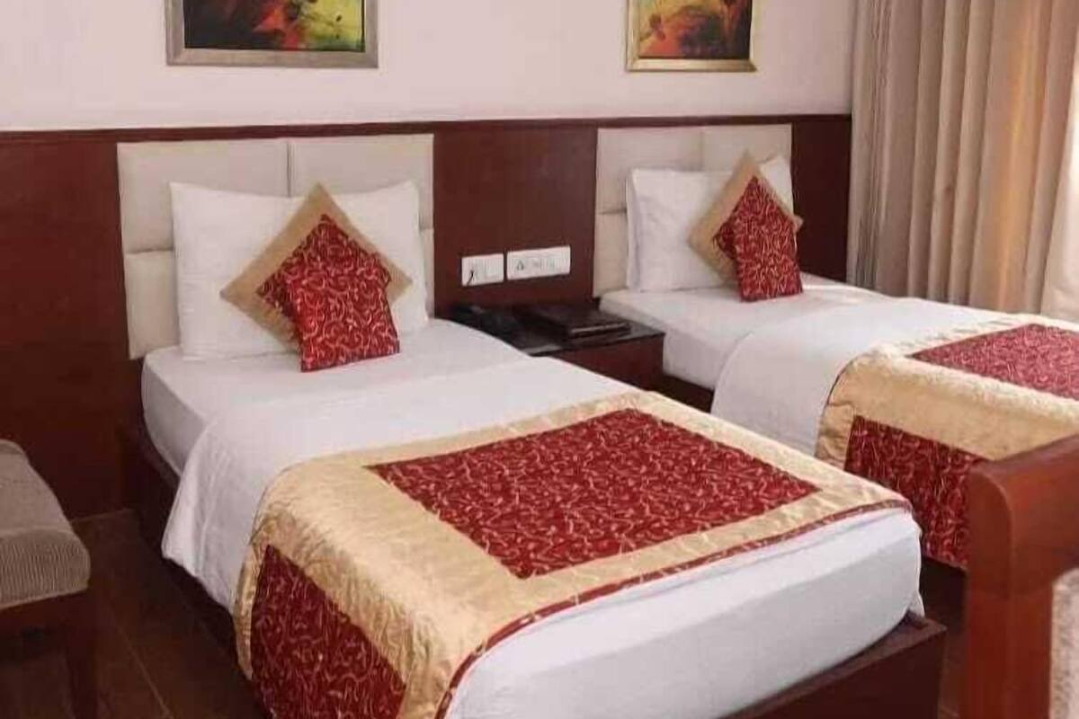 A hotel room with two beds, each with white linens and red patterned pillows. There are two paintings on the wall above the beds.